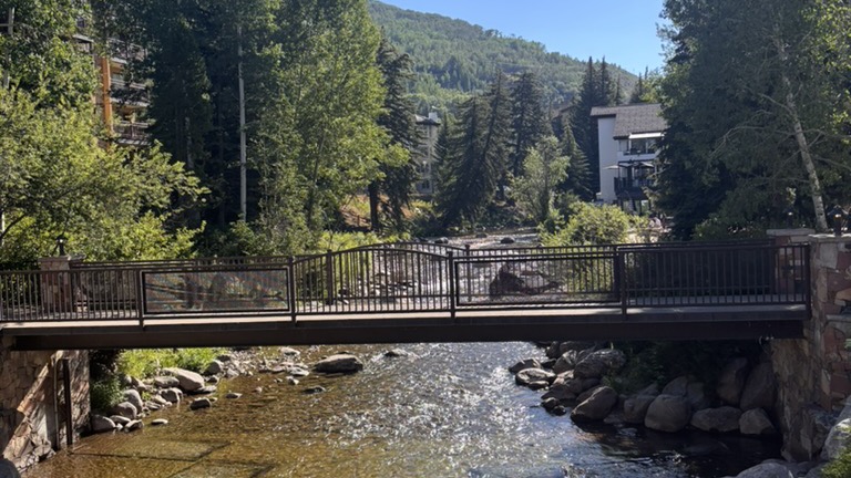 Un puente peatonal sobre Gore Creek en Vail, Colorado, rodeado de pinos y montaña, en el Eagle River Valley donde Doble AI trabaja con negocios locales